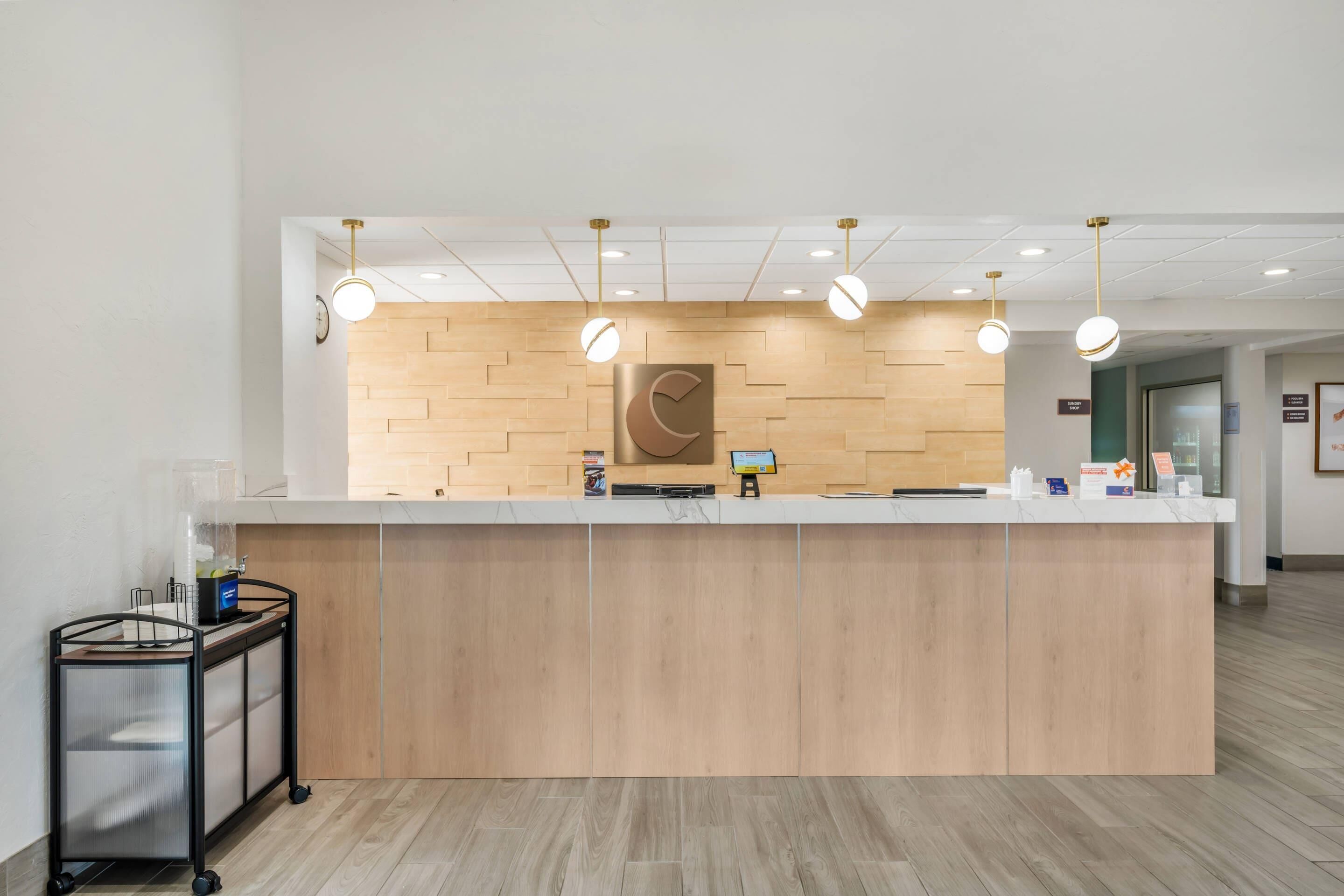 Un mostrador de recepción con paneles de madera, una vitrina de vidrio y un carrito con un ordenador.