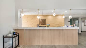 Un mostrador de recepción con paneles de madera, una vitrina de vidrio y un carrito con un ordenador.