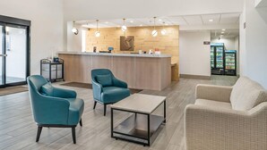 Un hall d’entrée moderne avec un comptoir de réception, des fauteuils bleu sarcelle et beige, une table basse et un réfrigérateur en arrière-plan.