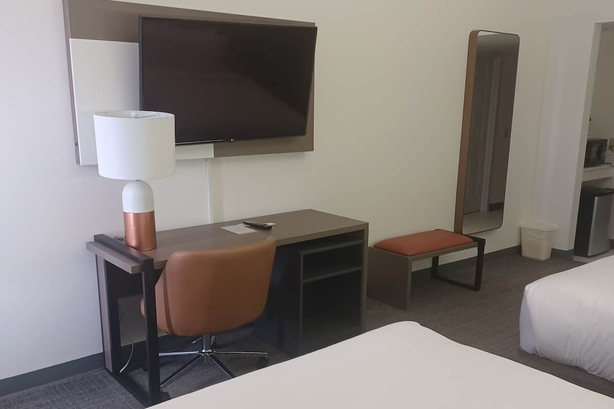 A hotel room with a bed, a desk with a chair, a television, a mirror, and a small table.