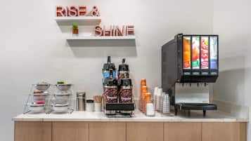 A coffee station with multiple coffee dispensers, a water dispenser, and a sign that reads "RISE & SHINE".