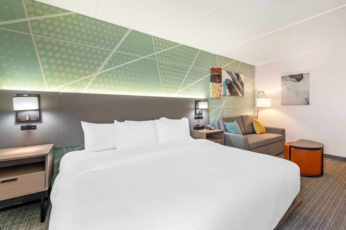 A hotel room with a large bed, a nightstand, a desk, a sofa, and a small side table.