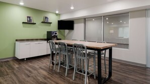 Een vergaderruimte met een lange tafel, vier stoelen, een witte kast, een flatscreen-televisie en een raam met uitzicht.