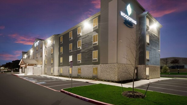 Een modern hotel met een opvallend 'Woodspring'-bord, een parkeerplaats en een verzorgd gazon.