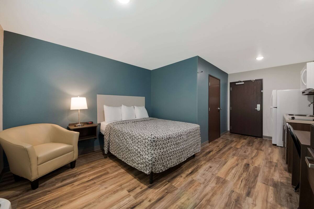 Una camera d'albergo con un letto, una sedia, una scrivania, una lampada e una porta.