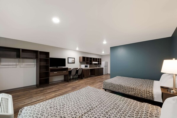 Una habitación de hotel moderna con dos camas, un escritorio, una silla, un microondas y un refrigerador.