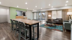 Een moderne hotelkamer met een houten eettafel, groene stoelen, een sofa en een salontafel.