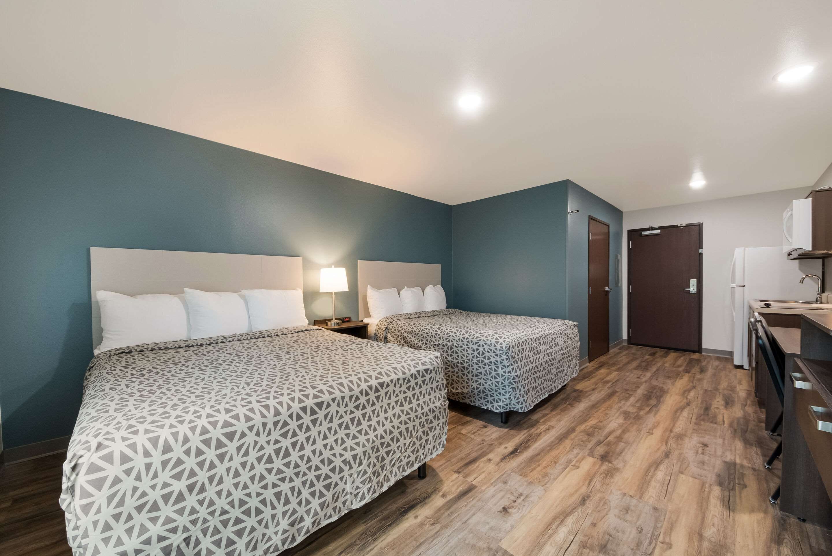 A hotel room with two beds, a wooden floor, a bathroom with a sink, and a door.