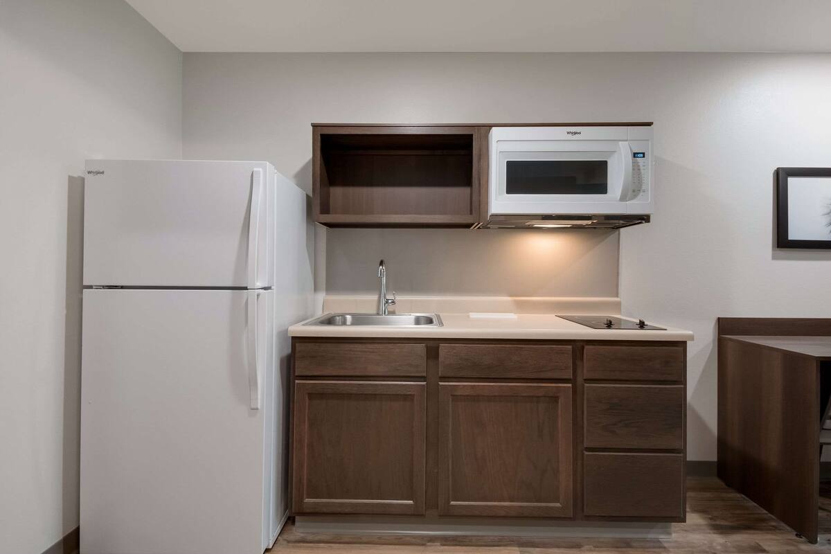 Una cucina compatta con frigorifero integrato, forno a microonde e lavandino con mobili in legno.