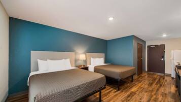 A hotel room with two beds, wooden flooring, and a blue accent wall.
