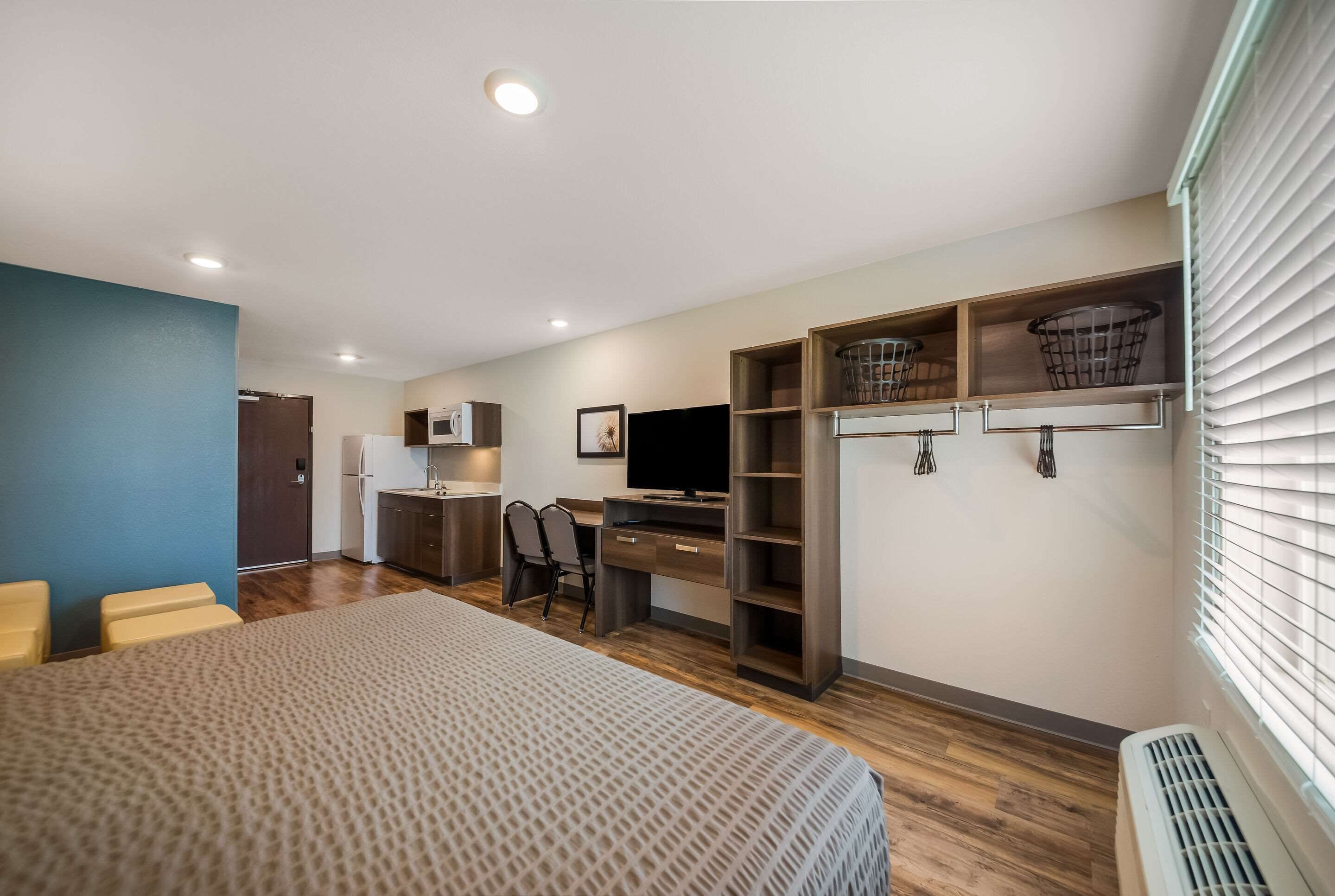 A modern bedroom with a bed, desk, TV, and built-in storage.