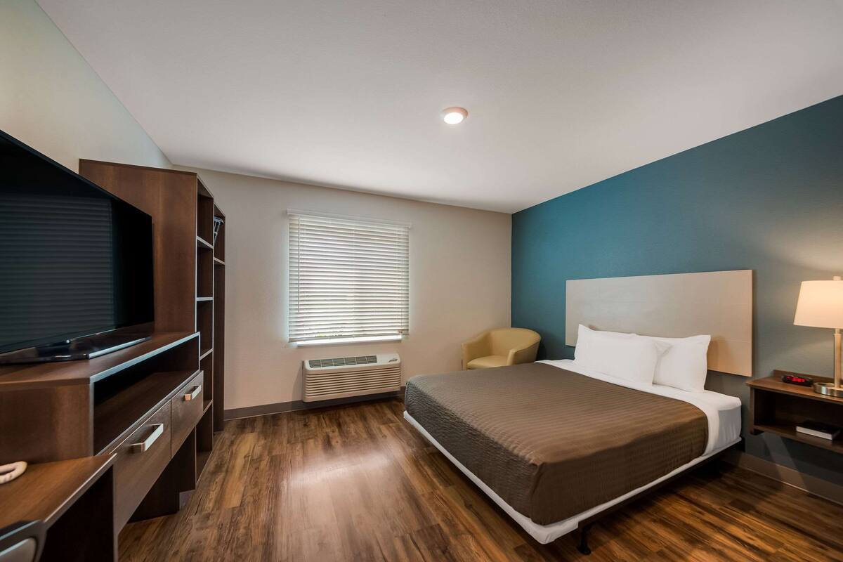 A hotel room with a bed, a TV, a desk, a chair, and a nightstand.