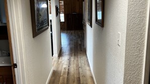 Ein Flur mit Holzboden, gerahmten Bildern an den Wänden und einer Tür zum Küchenbereich.