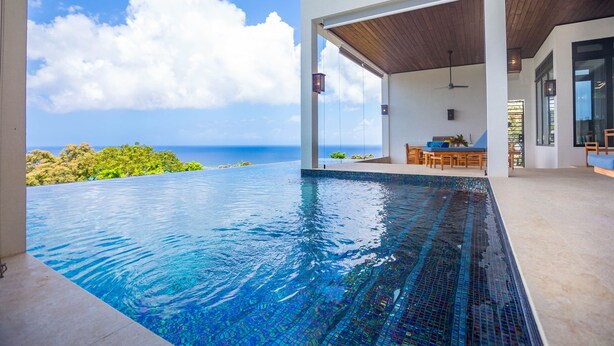Ein moderner Infinity-Pool mit freiem Blick auf den Ozean, einer Holzdecke und einem Essbereich mit Gartenmöbeln.
