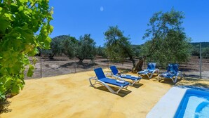 Zona de piscina con sillas reclinables azules y un cielo azul despejado.