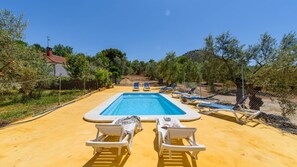 A rectangular pool with a clear blue water surface, surrounded by a sandy area with white lounge chairs and a fence.