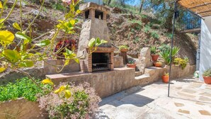 A stone-built outdoor kitchen with a chimney, surrounded by potted plants and a stone pathway.