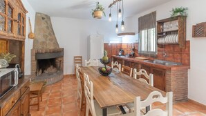 A kitchen with a stone fireplace, wooden dining table, and hanging light fixtures.