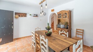 A dining area with a wooden table and white chairs, a fruit bowl, a vintage sewing machine, a wooden cabinet with a microwave, and a black door.