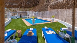 Ett område vid poolen med solstolar, en liten pool och en pergola som ger skugga.