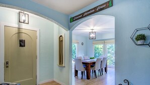 A dining area with a wooden table and chairs, a chandelier, and a view of trees through large windows. - Dunsmuir Adventure House ~ Spacious family getaway (Dunsmuir)