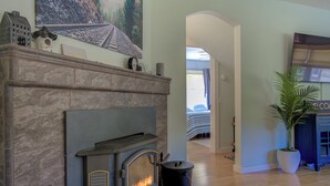 A fireplace with a stone mantle, a painting of a railway track, and a potted plant in a corner. - Dunsmuir Adventure House ~ Spacious family getaway (Dunsmuir)