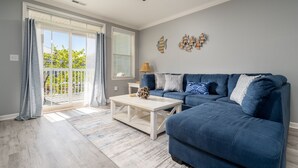 A living room with a blue sofa, a white coffee table, and a ceiling fan. - Beautiful Sunset Island 3 BR Condo, FREE Linens &Towels, includes 4 Beach Chairs (Ocean City)