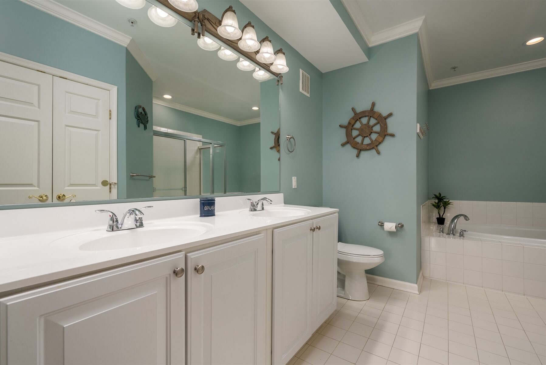 A bathroom with a double sink vanity, a toilet, a bathtub, and a large mirror.