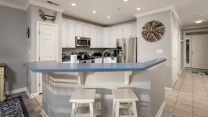 A modern kitchen with white cabinets, a blue countertop, stainless steel appliances, and a decorative wall piece. - Beautiful Sunset Island 3 BR Condo, FREE Linens &Towels, includes 4 Beach Chairs (Ocean City)