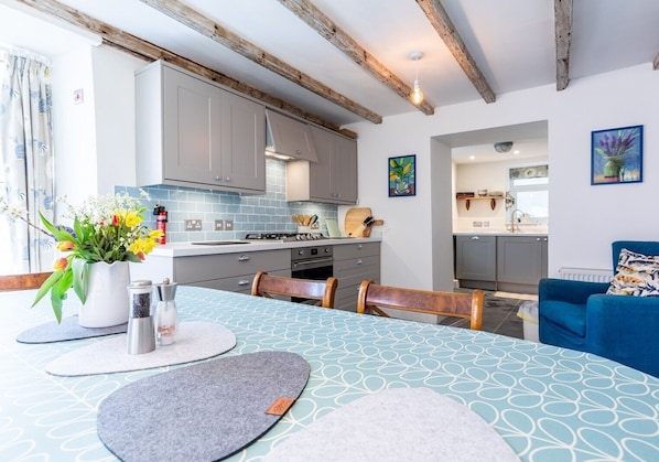A modern kitchen with grey cabinets, a blue tiled backsplash, and a dining area with a table set for two.