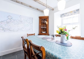 A dining room with a map on the wall, a wooden cabinet with glass doors, and a vase with flowers on the table.