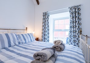 A neatly made bed with striped bedding, a bedside lamp, and a window with patterned curtains.