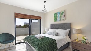 A modern bedroom with a bed, a nightstand, a chair, and a view of the outside. - Knightsbridge Terrace  (Cape town)