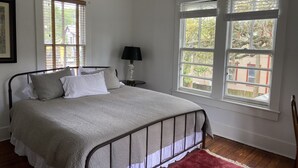 Ein Schlafzimmer mit einem Bett, zwei Fenstern, einer Lampe und einem roten Teppich.