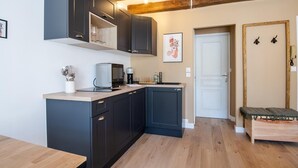 A compact kitchen with dark cabinets, a microwave, and a coffee maker. There is a wooden bench and a door with a gold frame.