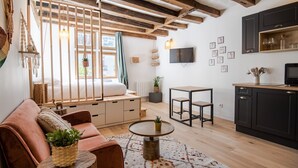 A cozy living room with a wooden ceiling, a sofa, a coffee table, and a kitchen area with cabinets and a TV.