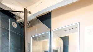 A modern bathroom with a glass-enclosed shower, a wooden vanity with a white sink, and a large mirror above the sink.