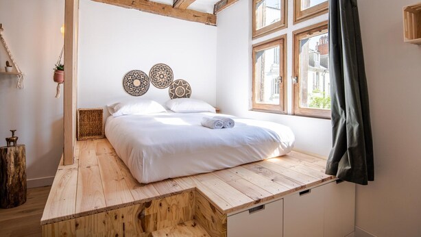 A bedroom with a wooden bed frame, a window with curtains, and decorative wall art.