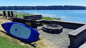 Area campeggio sul lago con un focolare, posti a sedere e un kayak blu.