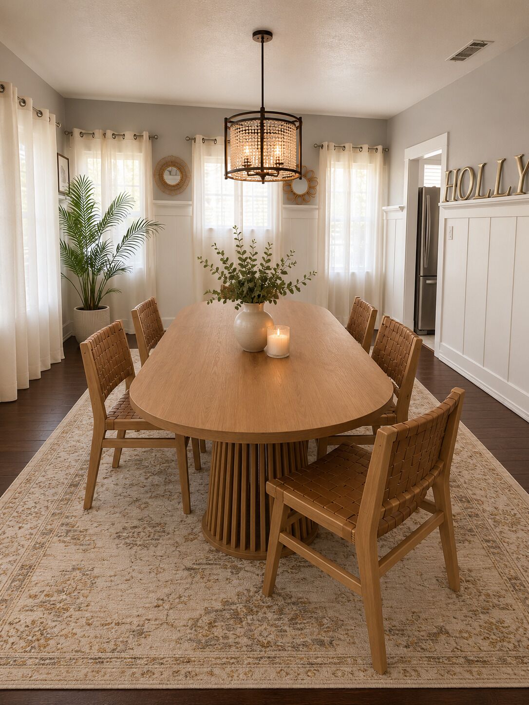 Une salle à manger avec une table ronde en bois entourée de six chaises, un lustre, une plante en pot et un tapis.