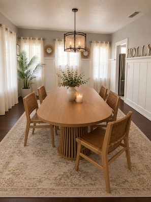 Une salle à manger avec une table ronde en bois entourée de six chaises, un lustre, une plante en pot et un tapis.