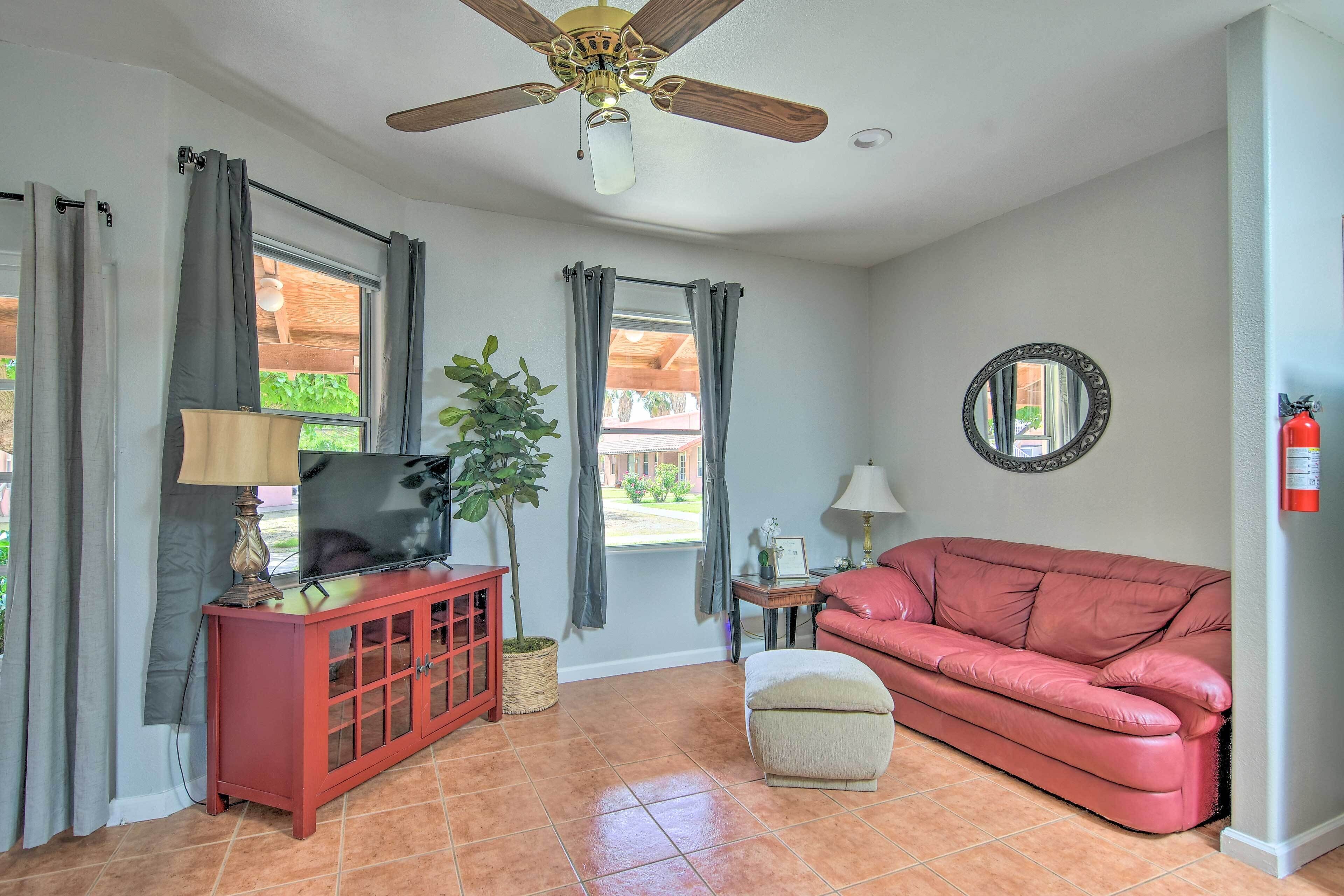 A living room with a red sofa, a television on a wooden cabinet, a ceiling fan, and a fire extinguisher on the wall.