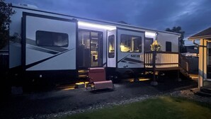 En stor autocamper med et køkken, en terrasse og et overdækket udendørs siddeområde.