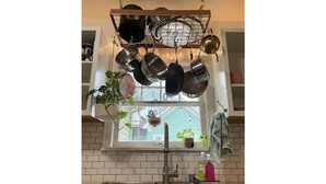 Een keuken met een hangende kruidenrek boven een raam, een spoelbak en een potplant.