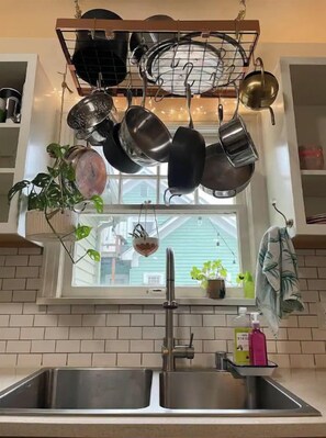 A kitchen with a hanging pot rack above a window, a sink, and a potted plant.