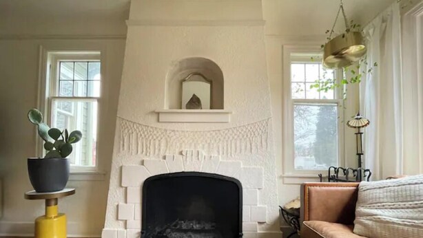 Een woonkamer met een witte openhaard, houten vloeren, een bruine leren bank en een potplant.
