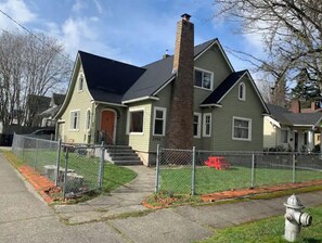Ein zweistöckiges Haus mit Schornstein, einer Veranda und einem eingezäunten Garten.