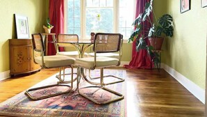 Een eetgedeelte met een tafel, stoelen, een kroonluchter, een raam met gordijnen en een kast.