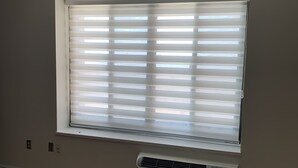 A room with a large window with blinds, a wall-mounted air conditioner, and a wooden floor. - Beach Getaway (Long Beach)