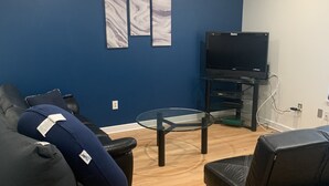 A modern living room with dark blue walls, a flat-screen TV, a glass coffee table, and two black sofas. - Beach Getaway (Long Beach)